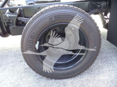 Truck wheel close-up showing spare tire mounted on rollback bed with black steel rim and tire sidewall text.