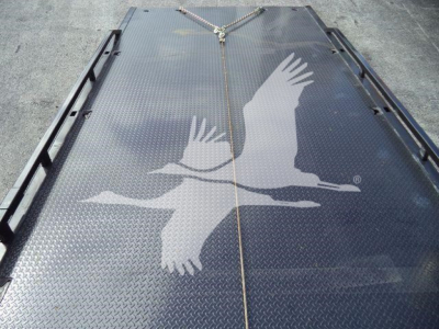 Flatbed or loading deck with diamond plate surface and a rope tied at center; large white gull graphic or stencil on metal surface.