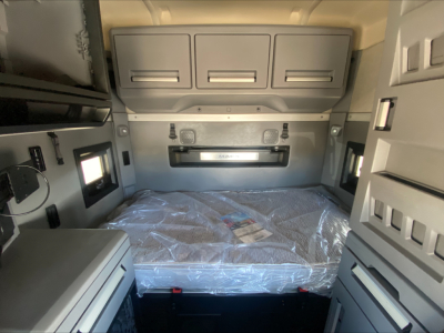 Inside a Mack AN64T70 truck sleeper cab showing overhead cabinets, small windows, and a wrapped mattress in the sleeping area.