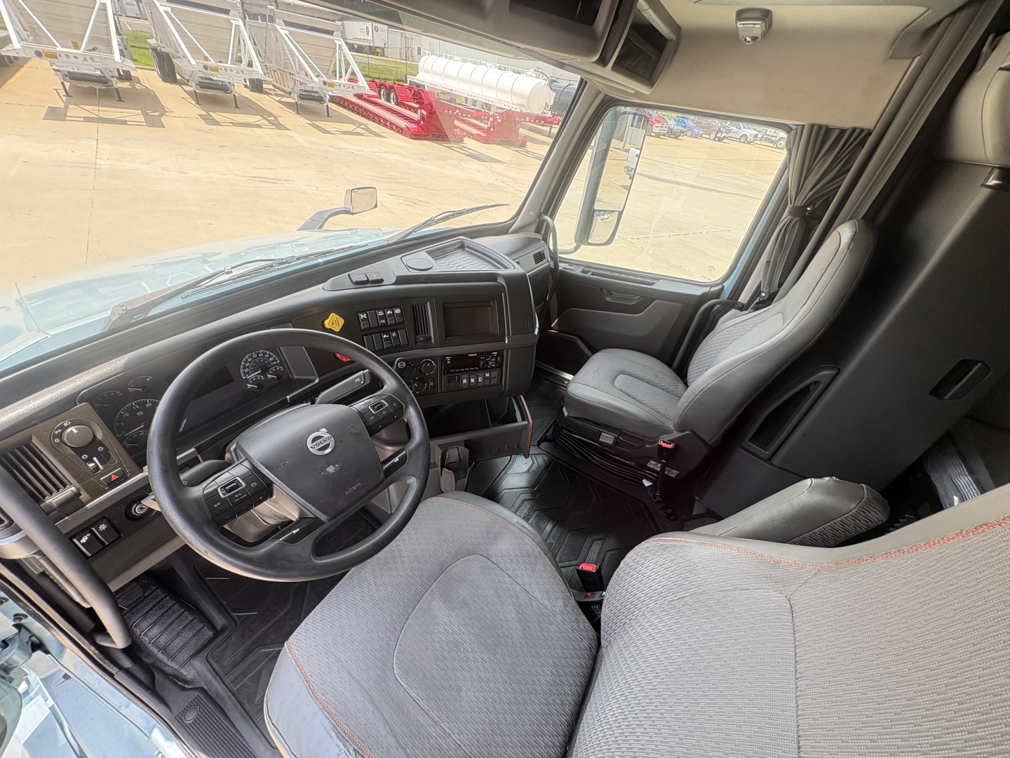 Volvo VNL interior showing steering wheel dashboard and driver seat with gray upholstery.