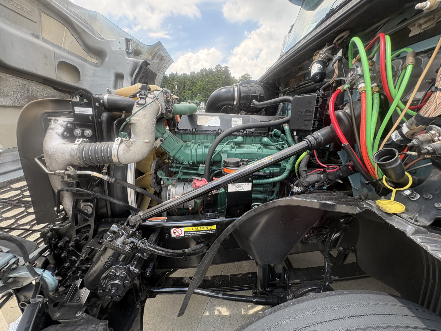 Volvo VNL64T760 engine bay with green engine, exposed hoses, wiring harnesses in foreground, and components such as coolant reservoir and turbocharger visible.