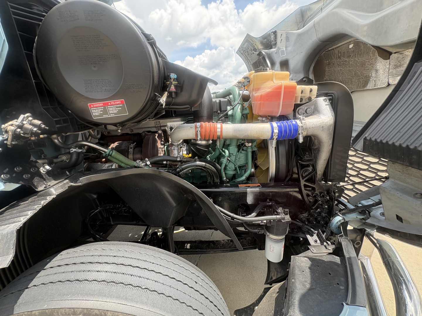 Truck engine bay of a 2022 Volvo VNL64T760 showing engine, hoses, reservoir caps, and components in a sleeper cab chassis.