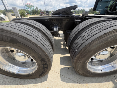 Dual rear tires on a Volvo truck chassis shown in a close-up view; visible are the tires and chrome rims, with a portion of the frame and fifth wheel in the background.
