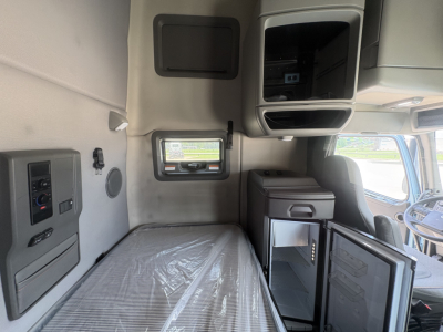 Volvo VNL64T760 sleeper cab interior showing side panel with controls, window, bunk bed, and small fridge cabinet.