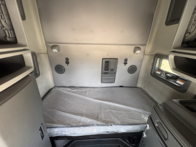Volvo VNL64T760 sleeper cab interior cargo area with bed platform and rear wall controls, two circular speakers, and side storage panels.