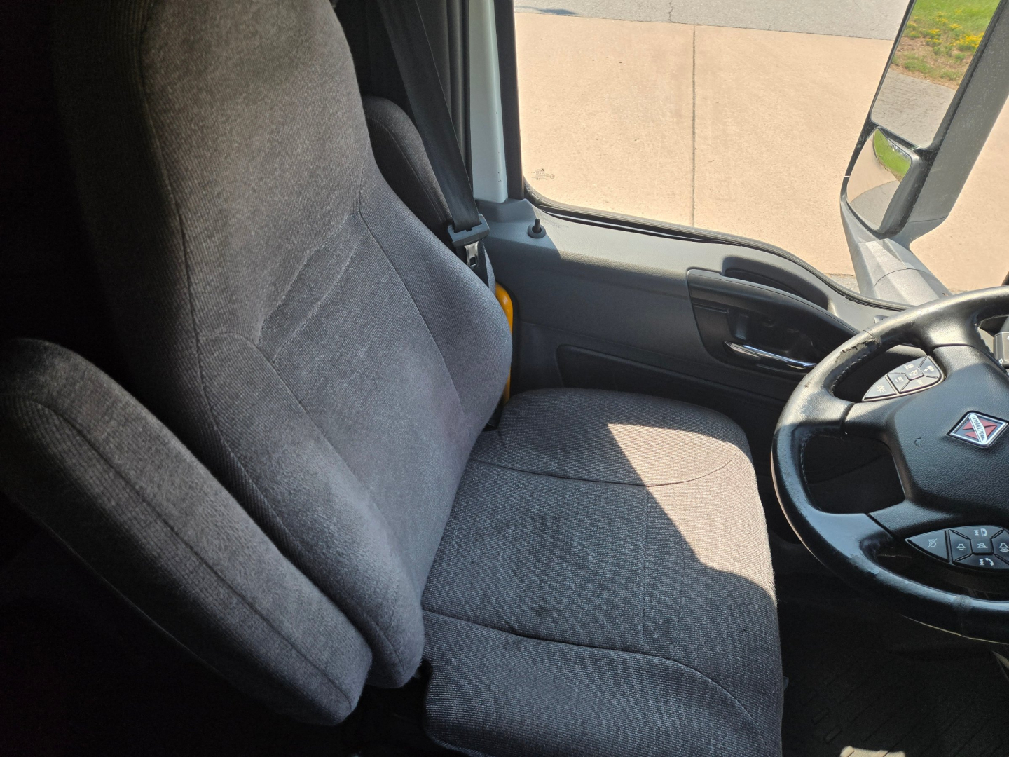Interior of a 2021 International LT625 truck cab showing driver seat and steering wheel; gray fabric seats; side window and door panel visible.