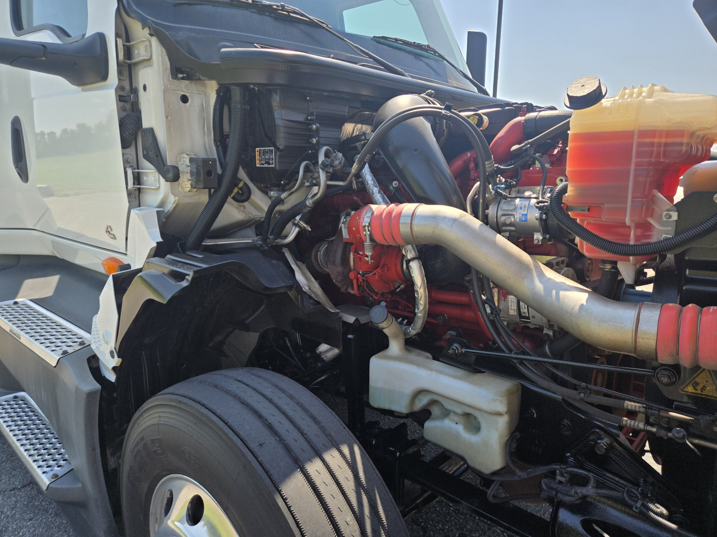 Truck engine bay of 2021 International LT625 showing air intake, coolant reservoir, hoses, and engine block with red components.