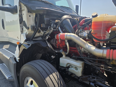 Truck engine bay of 2021 International LT625 showing air intake, coolant reservoir, hoses, and engine block with red components.