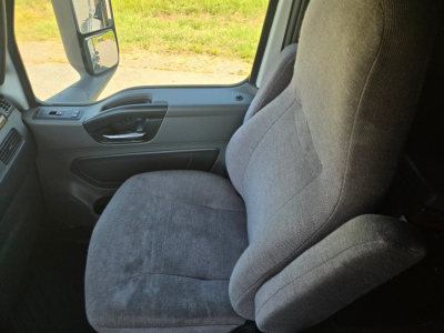 Interior close-up of a truck cab seat in a 2021 International LT625, gray fabric seat with armrest, window and dashboard visible.