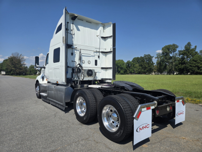 Truck rear-left view showing dual rear axles, fifth-wheel area, white sleeper cab, and mud flaps with MHC logo.