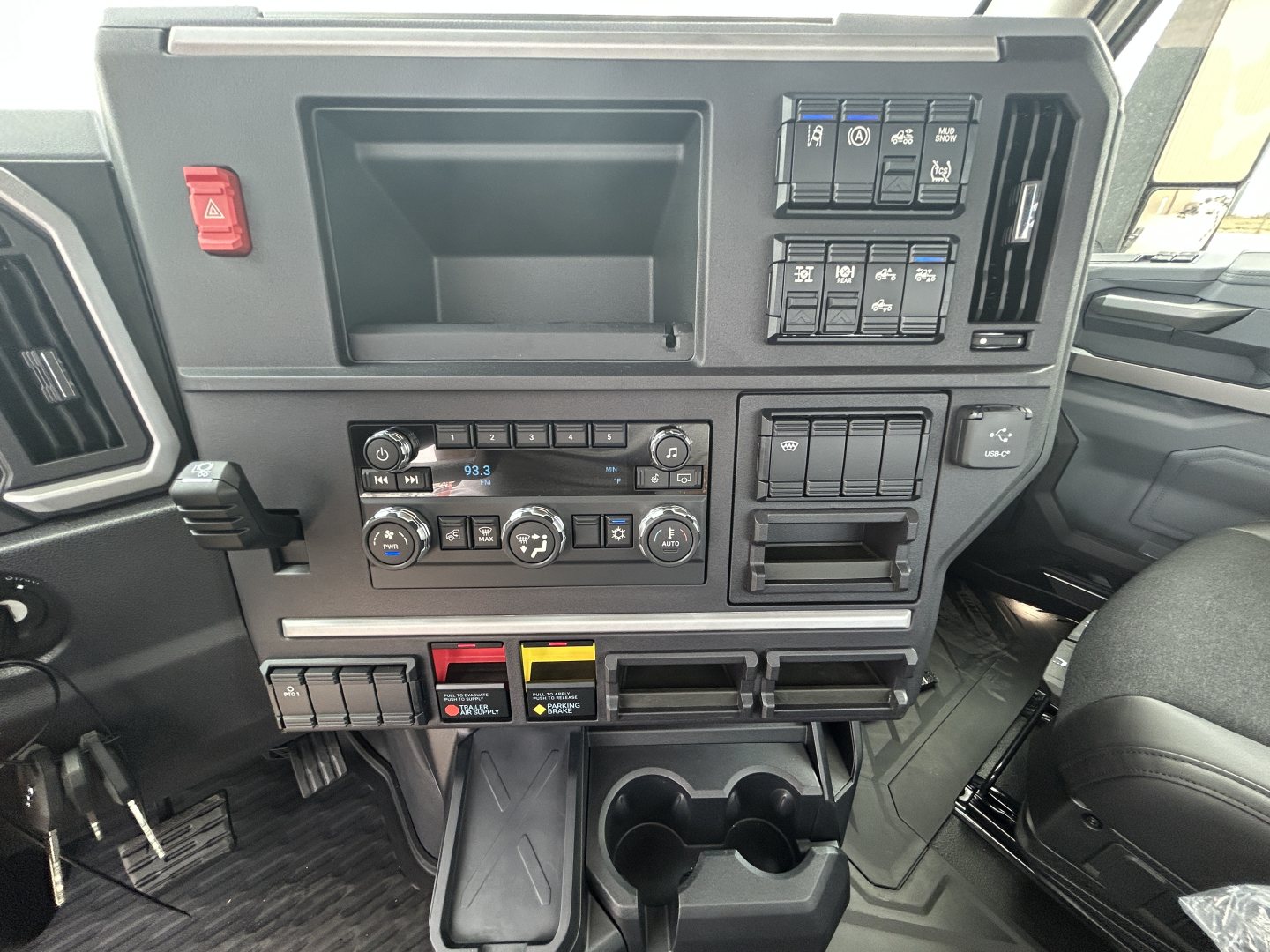 Dashboard of a new 2026 Mack PR64T showing controls, switches, cup holders, and storage compartments.