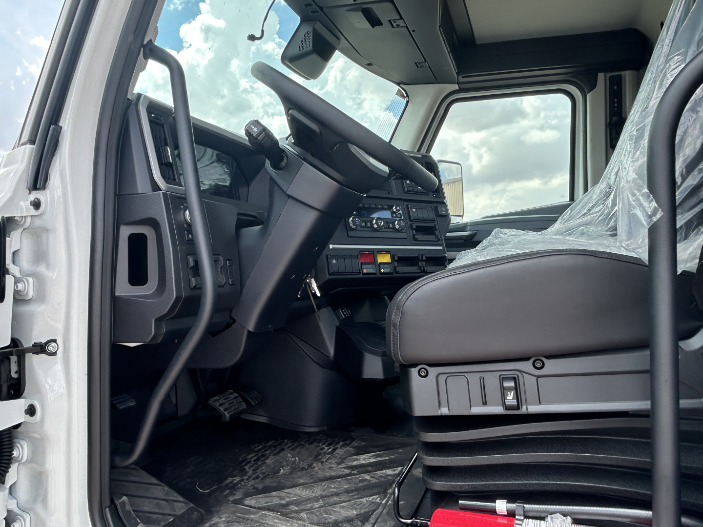 Mack PR64T truck cab interior showing steering wheel and dashboard with control panel, driver seat, and protective plastic on seat.