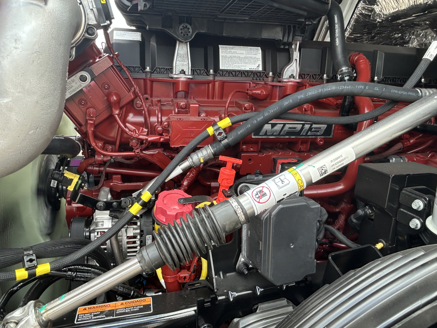 Mack PR64T engine bay showing red MPI6 diesel engine, hoses, and battery area with yellow and red caps.
