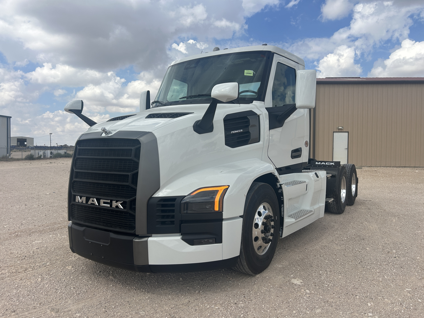 Mack PR64T truck front-left view showing white cab and black grille with Mack emblem, large side mirrors, and dual rear axles.