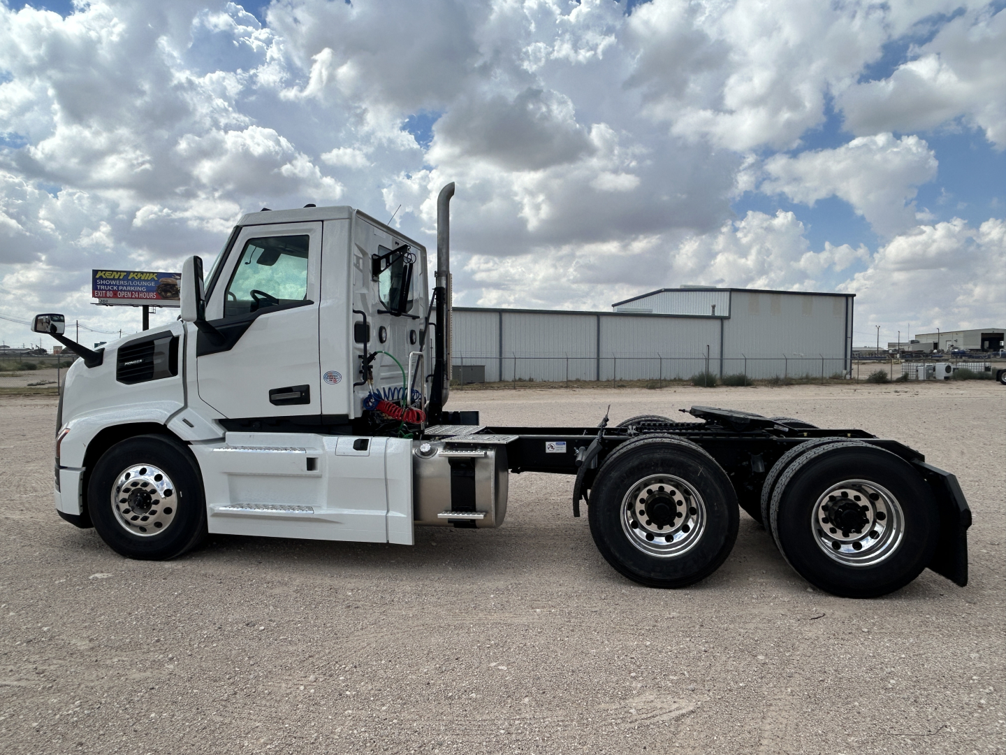 Mack PR64T truck chassis side view with cab, fuel tanks, and dual rear axles in a gravel lot.