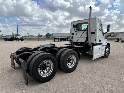 Mack PR64T conventional daycab tractor showcasing rear triple axles, chassis, and exhaust stack; visible VIN tag and cabin with white paint.