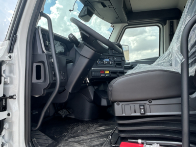 Mack PR64T truck cab interior showing steering wheel and dashboard with control panel, driver seat, and protective plastic on seat.