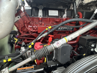 Mack PR64T engine bay showing red MPI6 diesel engine, hoses, and battery area with yellow and red caps.