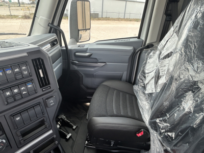 Truck interior front driver seat with plastic-wrapped seat, dashboard with controls, side door, and large side mirror.