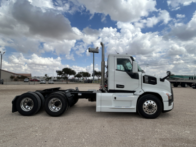 Front half view of a white 2026 Mack PR64T conventional daycab truck, side profile exposed with triple rear axle, no trailer, clear sky.