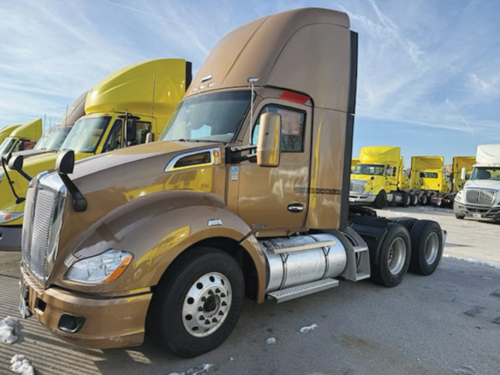 Kenworth T680 conventional daycab tractor showing cab and side exhaust, brown color with chrome fuel tanks and wheels; multiple yellow trucks in background.