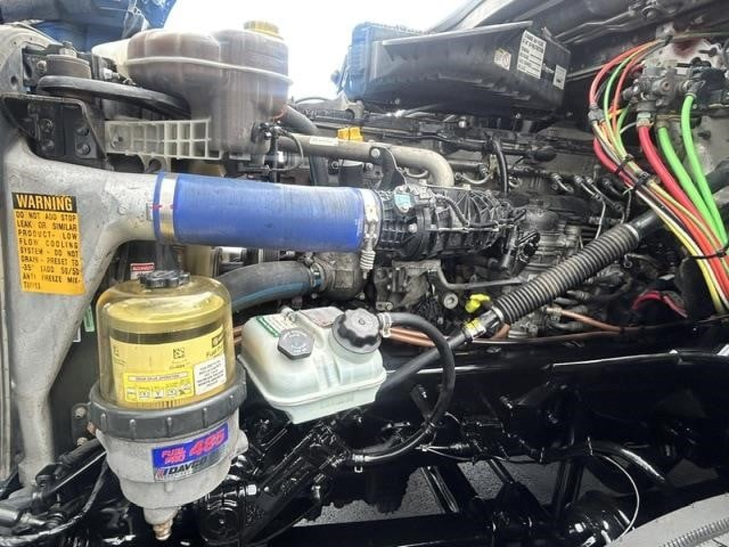 Freightliner Cascadia 126 engine bay showing blue coolant hose, yellow reservoir, and wiring harness with labels.