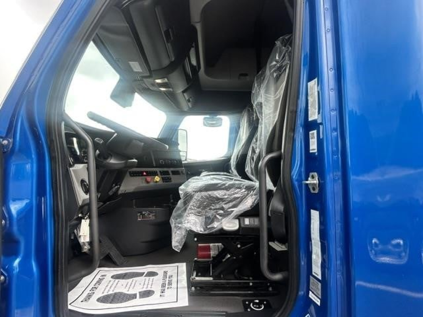 Freightliner Cascadia 126 truck interior cab view showing driver's seat and dashboard with plastic seat cover and steering wheel.
