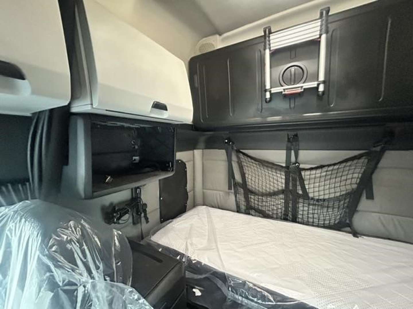 Freightliner Cascadia sleeper cab interior showing bunk area with mattress, overhead cabinet, and cargo net.