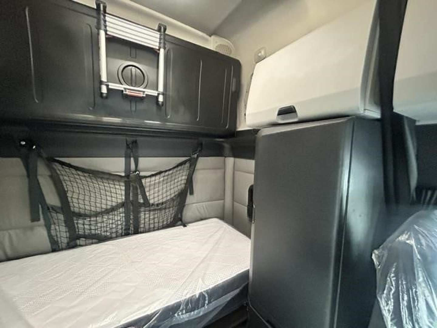 Freightliner Cascadia sleeper cab interior with upper bunk storage cabinet, netted storage, and mattress visible.