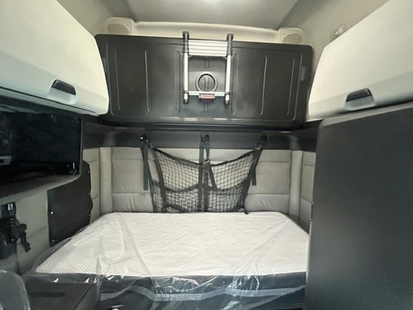 Cab interior of a Freightliner Cascadia sleeper cab showing bunk area with net storage on rear wall and overhead storage compartment.