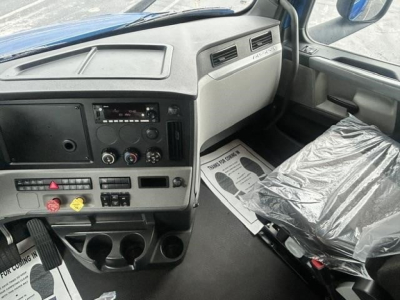 Truck dashboard interior of a 2022 Freightliner Cascadia 126 with grey cabin, steering area, center console, and plastic-covered seat.