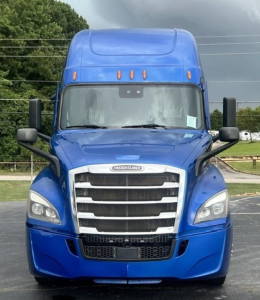 Front view of a blue Freightliner Cascadia 126 tractor, cab with grille, headlights, mirrors; appears in a dealership lot.