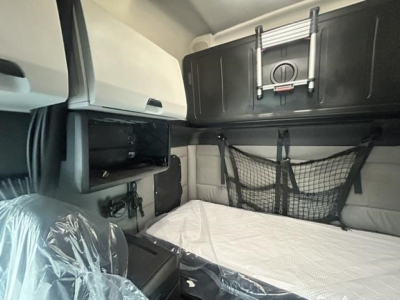 Freightliner Cascadia sleeper cab interior showing bunk area with mattress, overhead cabinet, and cargo net.
