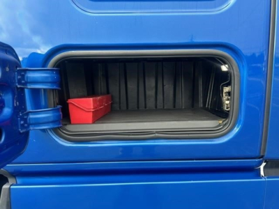 Cabin storage compartment on blue Freightliner Cascadia shows empty under-bunk area with small red bin inside.