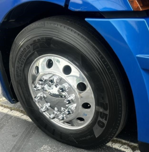 Truck wheel close-up showing polished steel hub with lug nuts and Bridgestone tire on a blue Freightliner Cascadia 126.
