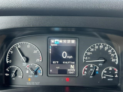 Freightliner Cascadia dashboard with digital speedo reading 0 mph, central display shows 63 F, 414,973 mi, and ECO/gear indicators. Left gauges include oil, battery; right gauges include coolant temp and fuel.