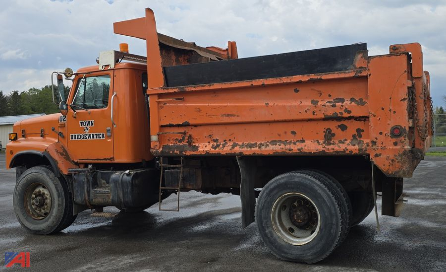 Dump truck side view showing orange International 2674 dump bed with black tailgate and worn exterior.