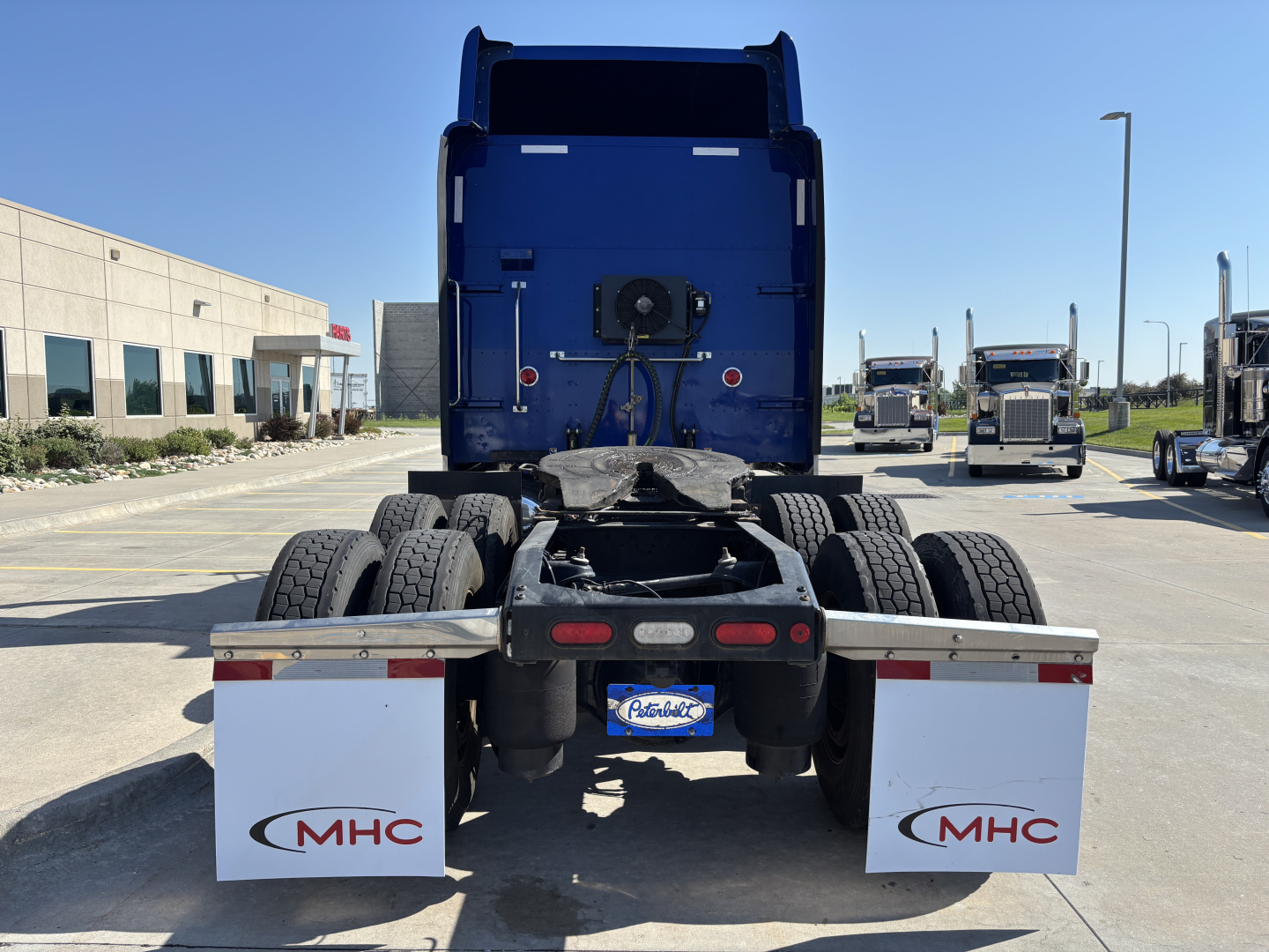 Truck rear view of a 2022 Peterbilt 389 conventional sleeper tractor showing dual rear axles, mudflaps with MHC logo, and blue sleeper with fifth wheel. VIN 1XPXD49X7ND789918 visible in context.
