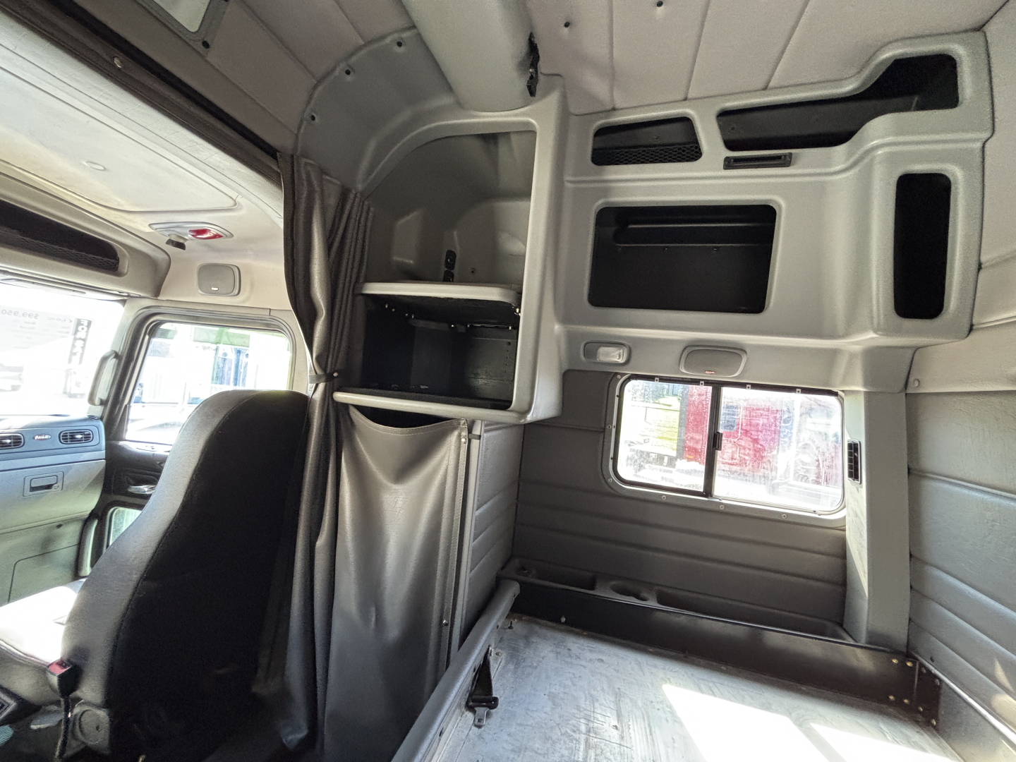Truck cab interior view of a 2022 Peterbilt 389 sleeper showing upper storage cabinets and windows.
