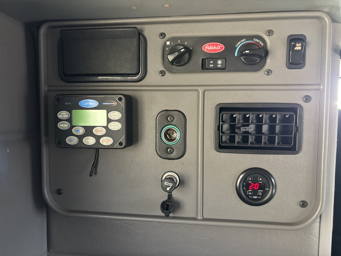 Peterbilt 389 dash area showing Ashkit heater/AC controls, CB radio, ignition, 12V outlet, gauge, and air vent