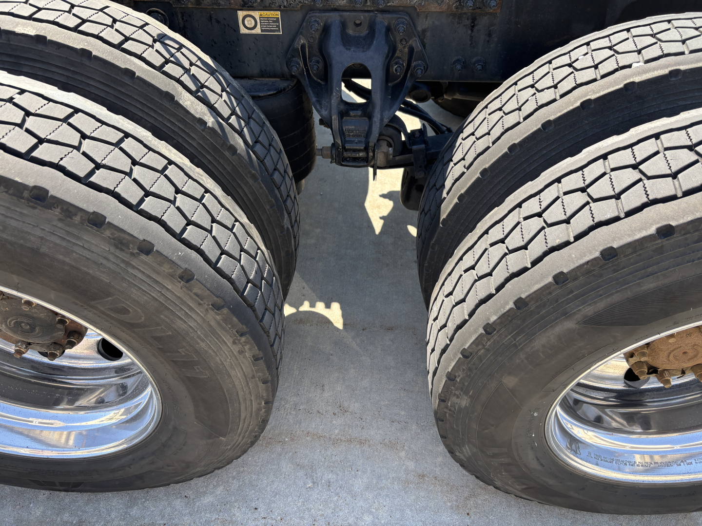 Dual rear tractor tires of a Peterbilt 389 chassis showing the tire treads and hub rims with a view of the fifth wheel and undercarriage.