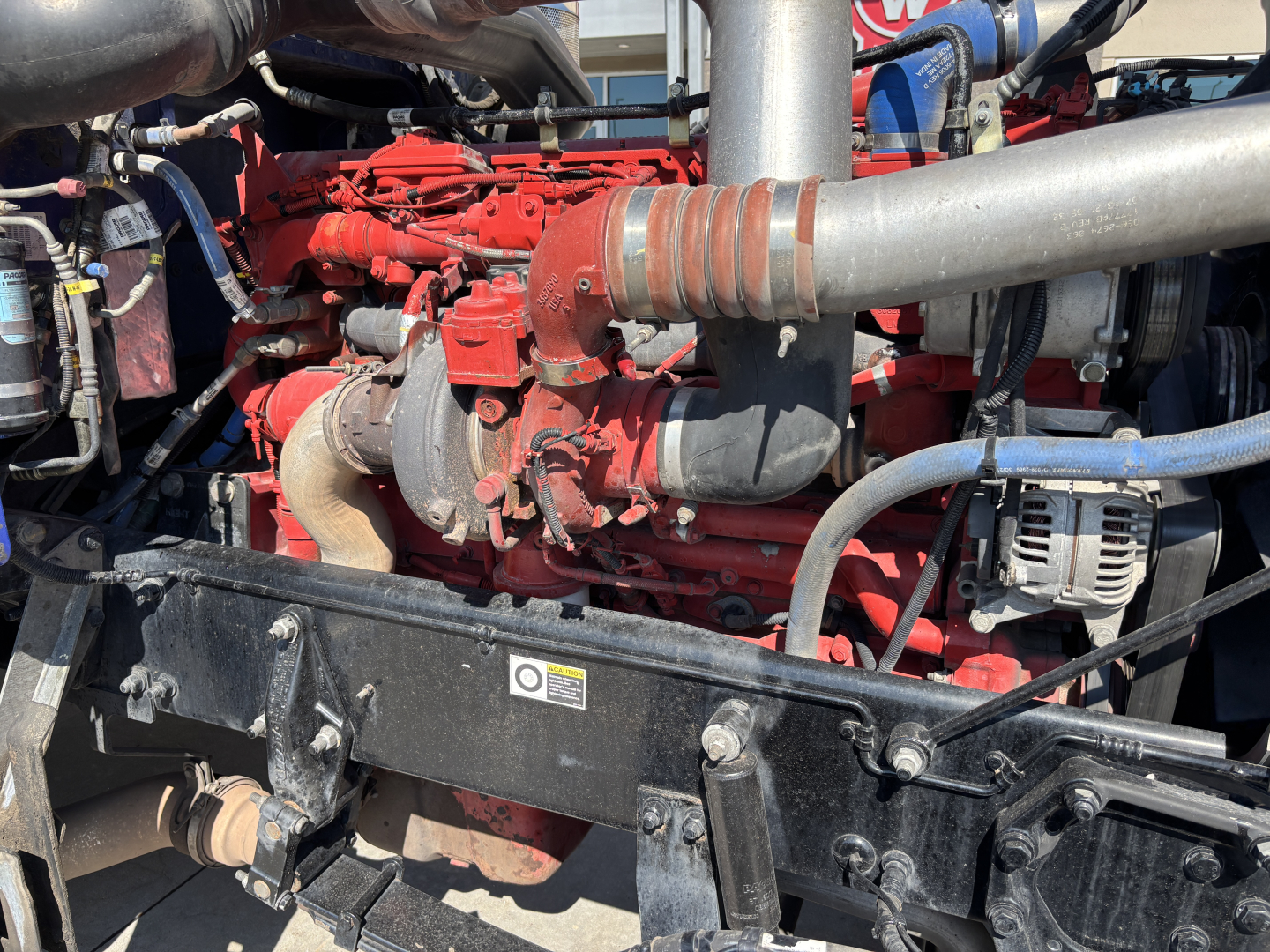 Peterbilt 389 engine bay view showing red engine components and intake piping.