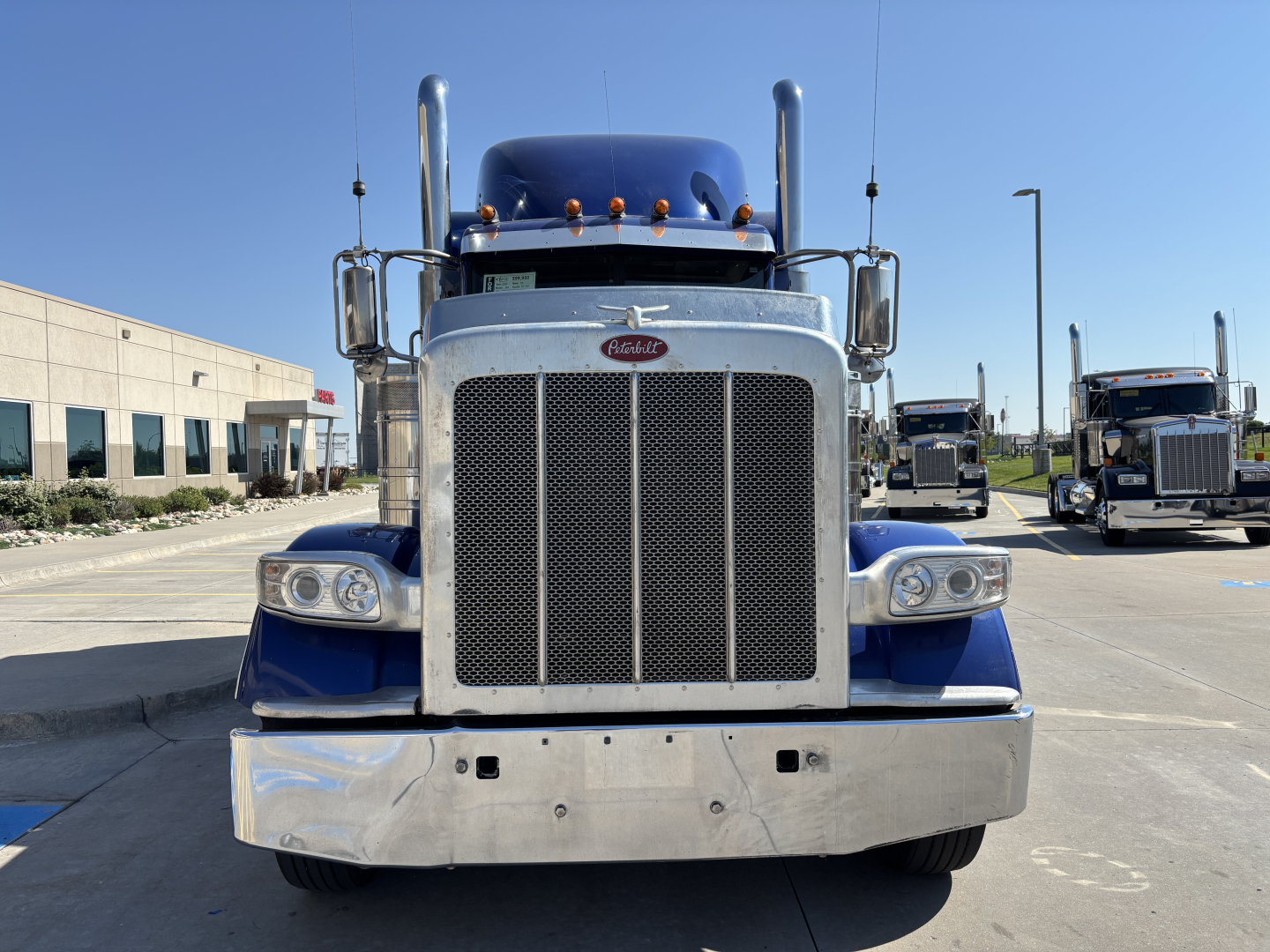 Peterbilt 389 conventional sleeper truck front view with large chrome grille and bumper, blue fenders, dual exhaust stacks, and twin headlights.