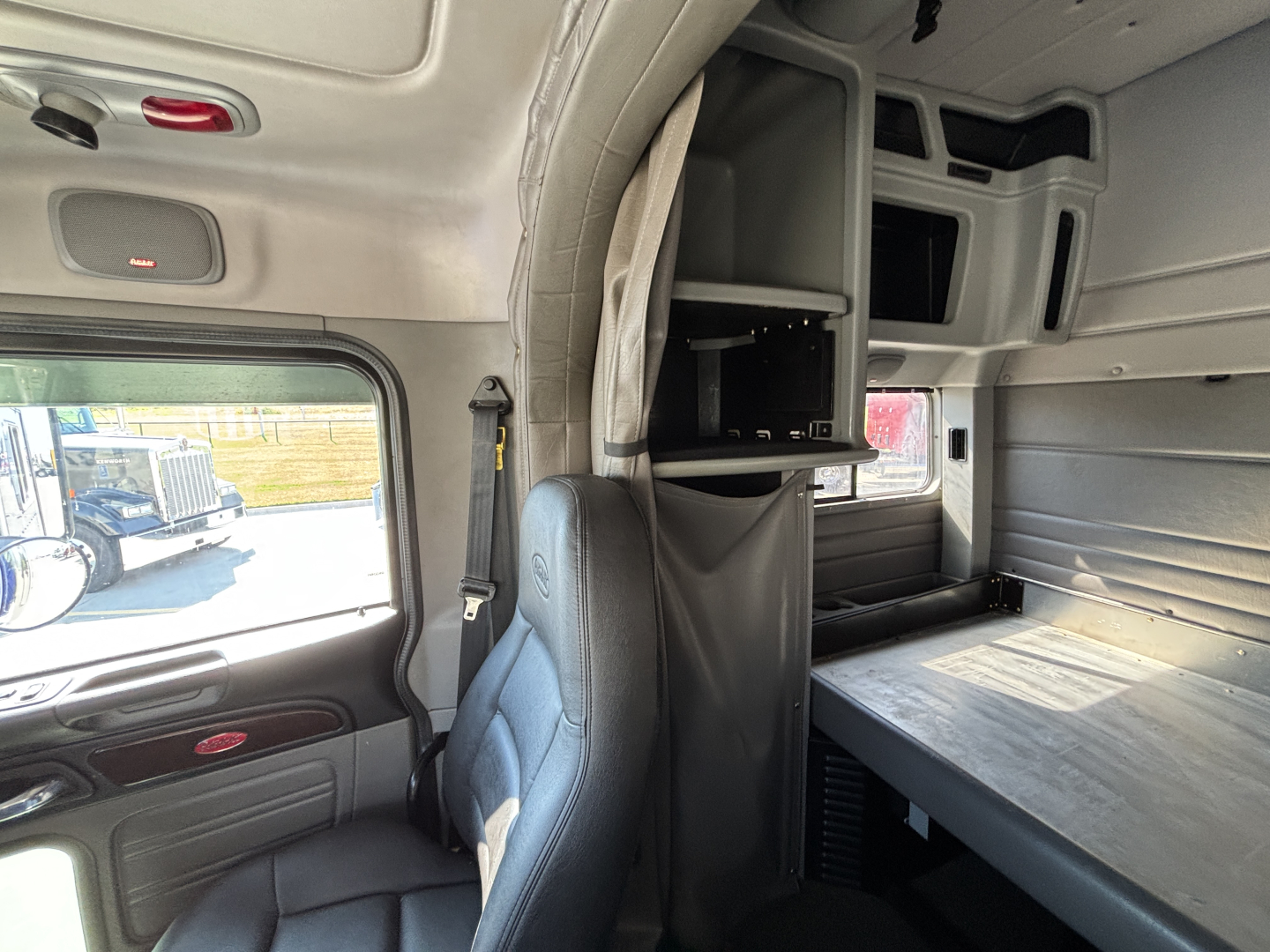 Peterbilt 389 sleeper cab interior showing upper bunk storage and work desk area with cabinets.