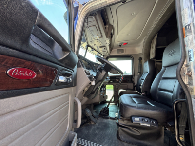 Peterbilt 389 cabin interior showing driver seat and dashboard with Peterbilt emblem on door panel.