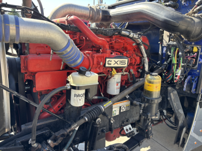 Peterbilt 389 engine bay with CX15 badge, red engine block, blue silicone hoses, multiple filters and yellow oil canister visible.