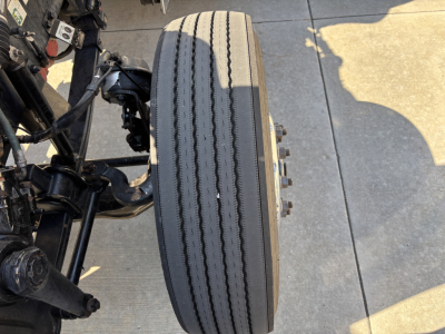 Peterbilt 389 truck front wheel and suspension showing tire with dual tread wear and wheel hub.