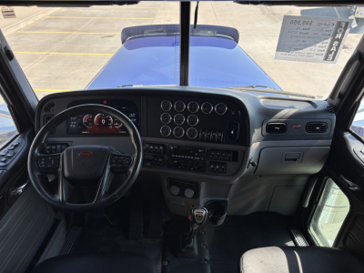 Peterbilt 389 interior dashboard and steering wheel view showing gauge cluster, multiple round gauges, and manual transmission shifter.