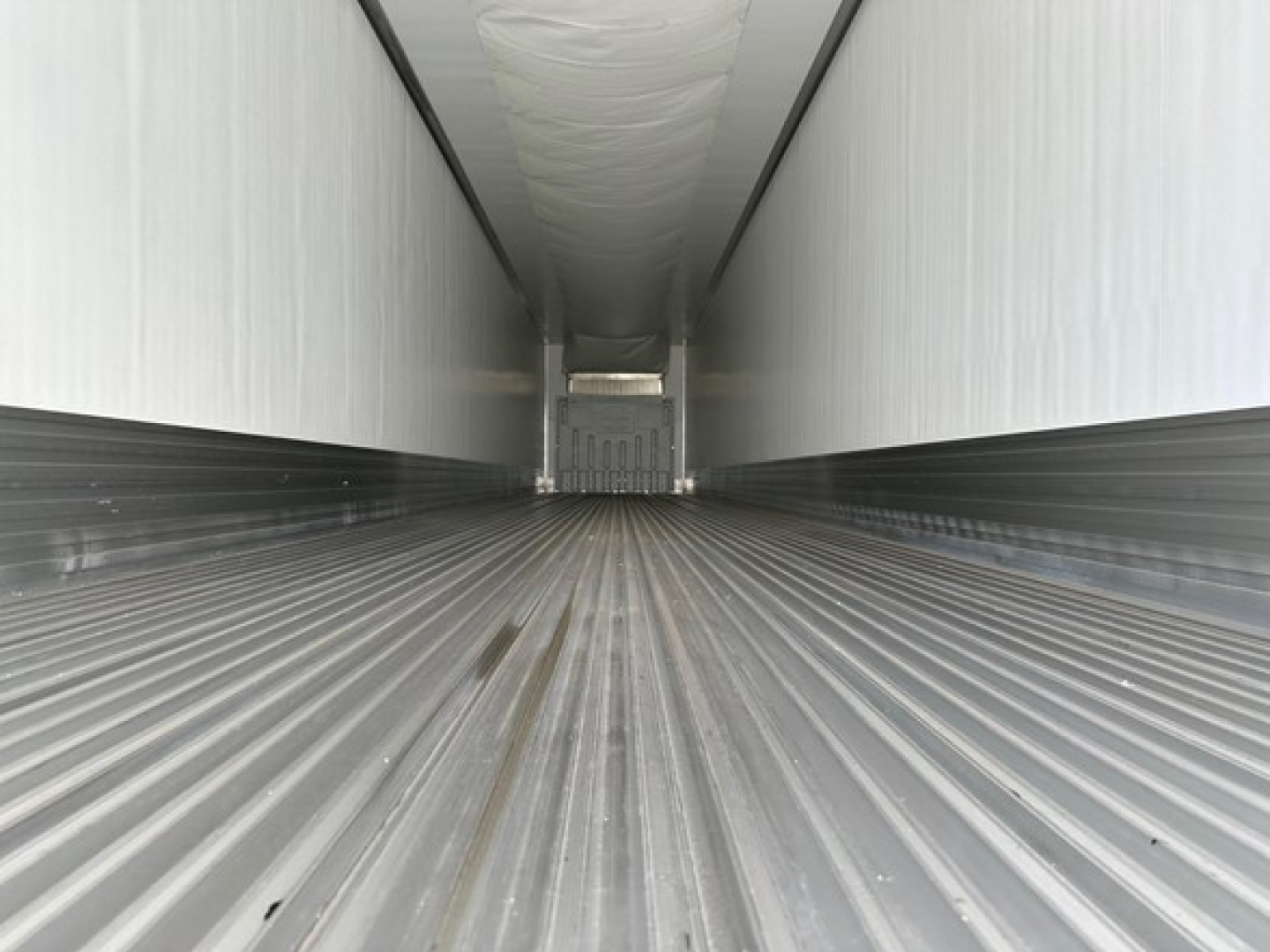 Trailer interior view showing empty refrigerated trailer with ribbed floor and white insulated walls.