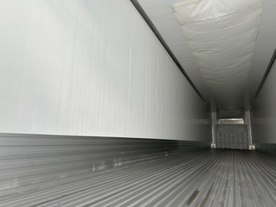 Empty reefer trailer interior with ribbed floor and side walls, rear doors visible in distance.
